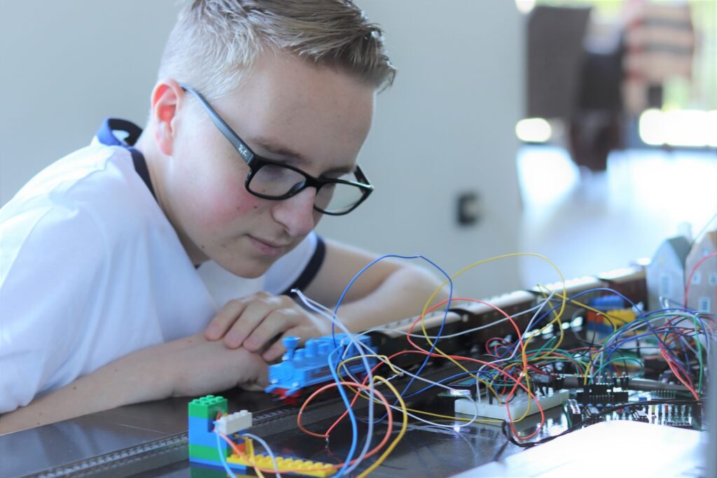 Boy engaged with electronic project involving toy train and wires indoors.